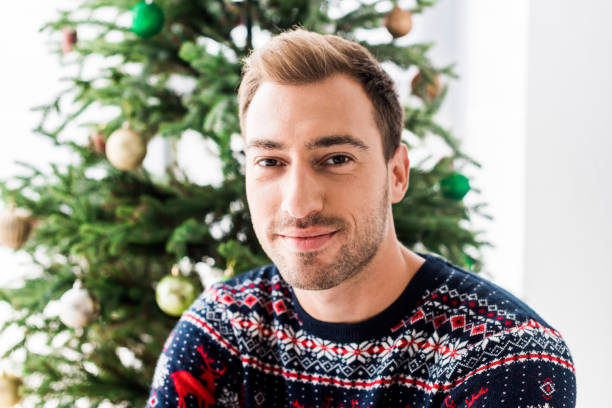 istock man in christmas sweater against christmas tree 1042968426