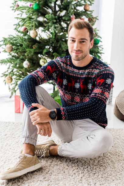 istock handsome man in winter sweater sitting near christmas tree 1042968444