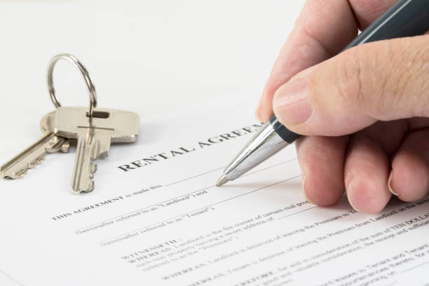 hand is writing with a pen on a rental agreement document, house keys in the background hand is writing with a pen on a rental agreement document, house keys in the background, selected focus, narrow depth of field lease agreement stock pictures, royalty-free photos & images