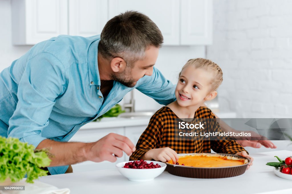 padre felice e adorabile bambina decorare torta di zucca ringraziamento insieme - Foto stock royalty-free di Cucinare