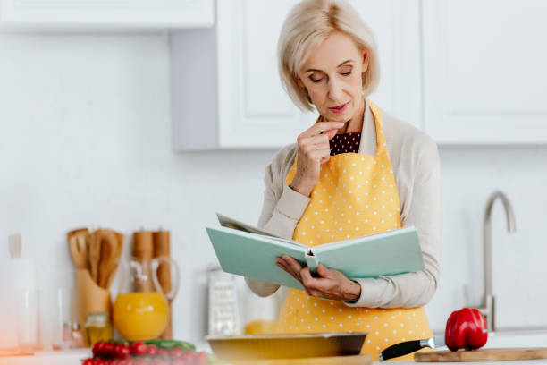 istock senior woman reading recipe book while cooking at kitchen 1042990098