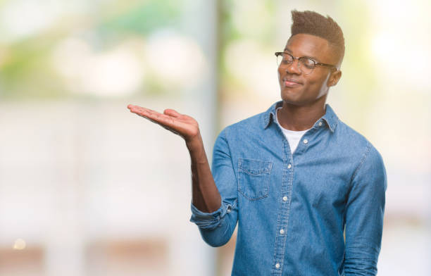 istock Young african american man over isolated background smiling cheerful presenting and pointing with palm of hand looking at the camera. 1042999572