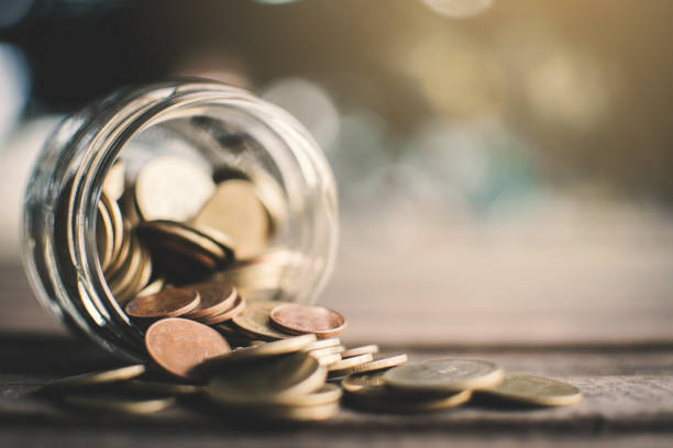istock Close-Up Of Coins Falling From Glass Jar On Table 1043003342