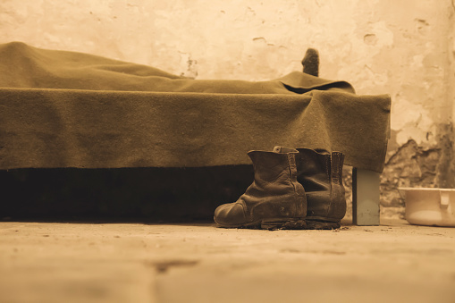 One person sleeping in a humble bedroom with a pair of old boots on the floor