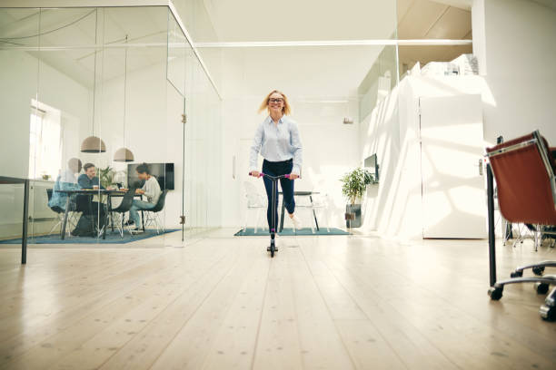 istock Young businesswoman laughing while riding a scooter in an office 1043032802