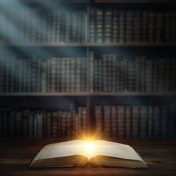 istock Open old book, magic light and the rays of light on a bookshelf background . 1043035316