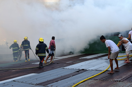 San Pablo City, Laguna, Philippines - September 22, 2018:Firemen and Civilian volunteers gather on rooftop put out fire using fire hose during house fire that gutted interior shanty houses