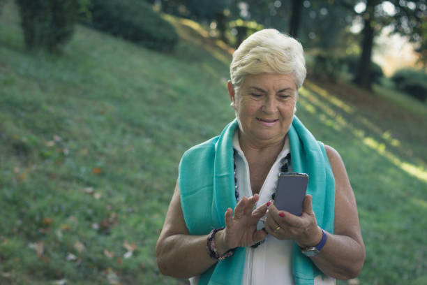 istock Young looking elder woman using cellphone at park 1043041194