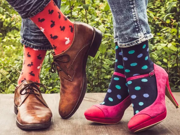 Legs of a young couple in stylish shoes, bright, colorful socks on the wooden terrace on the background of green trees. Lifestyle, fashion, beauty, fun