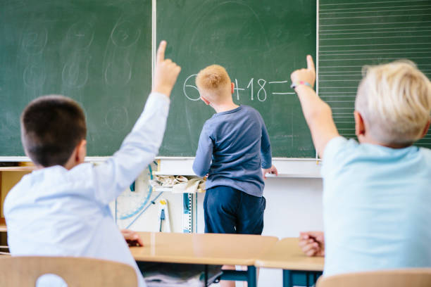 a boy stands in front of the blackboard and think about the task. while two boys are watching