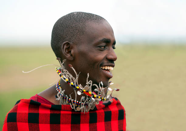 Maasai tribal warrior, Masai Mara National Park, Kenya, Africa. Maasai man in colourful traditional national costume with multicoloured beaded necklaces dancing, Masai Mara, Kenya, Africa