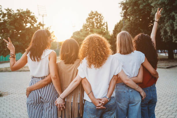 gruppo di amiche che si tengono per mano insieme contro il tramonto - woman with arms raised back view foto e immagini stock