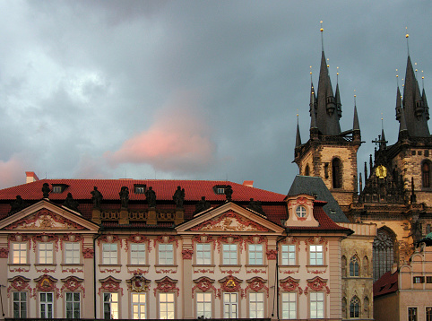 A gothic church and a palace, side-by-side on Wenceslas square, in Prague. On the twilight sky there is a pink cloud