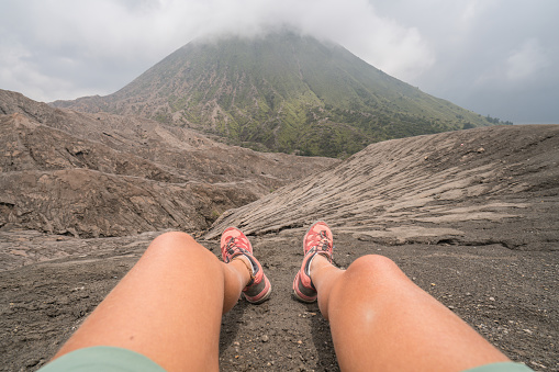 Personal perspective of woman hiker resting on mountain trail on crater volcano, Bromo national park view, on top of it all. People travel discovery concept \nIndonesia
