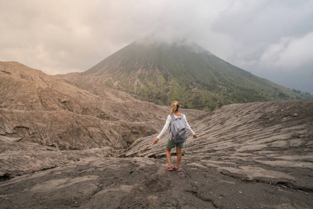 junge frau wandern steht, die arme ausgestreckt auf berg mit blick auf vulkane bromo in indonesien - menschen reisen spaß abenteuer konzept und erfolg - bromo crater stock-fotos und bilder