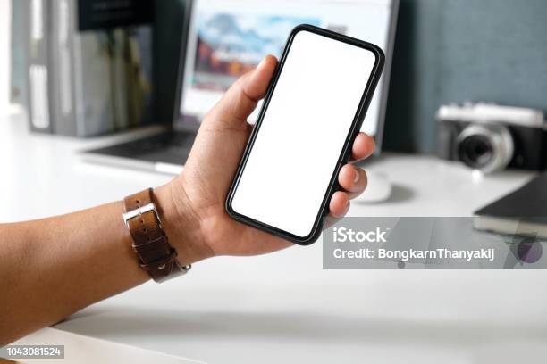 Cropped Shot A Mans Hand Holding Blank Screen Mobile Phone On Desk Stock Photo - Download Image Now