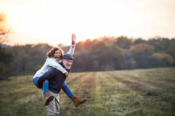 Photo of Senior man giving a woman a piggyback ride in an autumn nature.