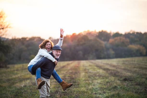 starszy mężczyzna dając kobiecie przejażdżkę piggyback w jesiennej naturze. - women autumn people leaf zdjęcia i obrazy z banku zdjęć