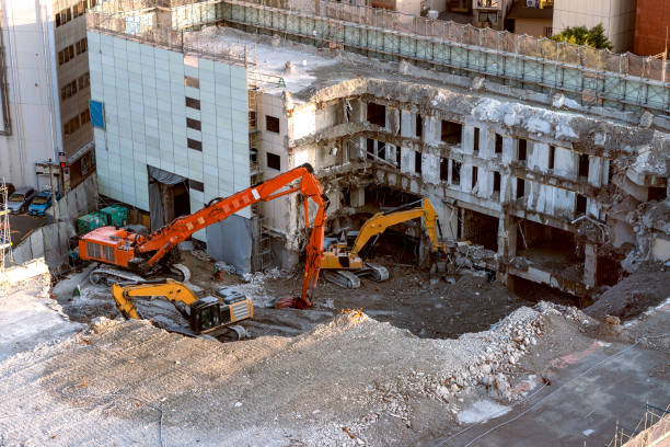 A building in the midst of being demolished with construction equipment in front..