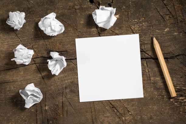 Blank white note paper with a pencil and some crumpled papers on wooden surface
