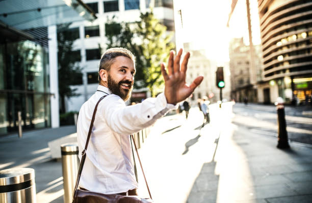 Hipster businessman walking up the street in London, looking back and greeting somebody. Rear view of hipster businessman walking up the street in London, looking back and greeting somebody. Copy space. waving gesture stock pictures, royalty-free photos & images