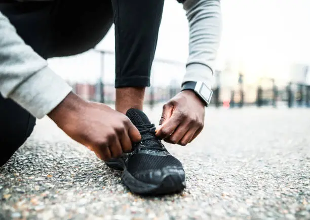 Photo of A close-up of a young sporty black man runner tying shoelaces outside in a city.