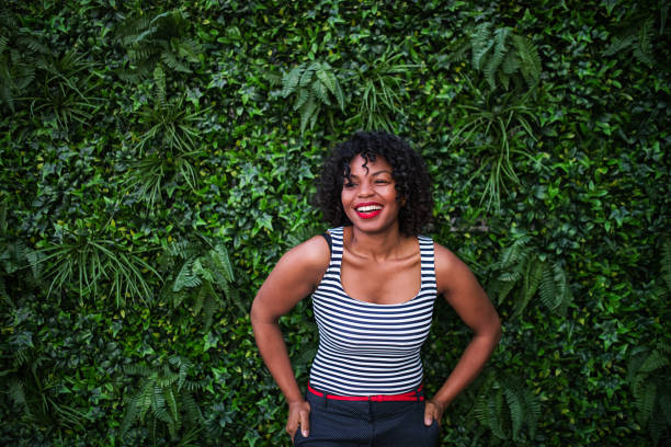 portrait d’une femme noire, debout sur un fond vert des feuilles de bush. - sans manches photos et images de collection