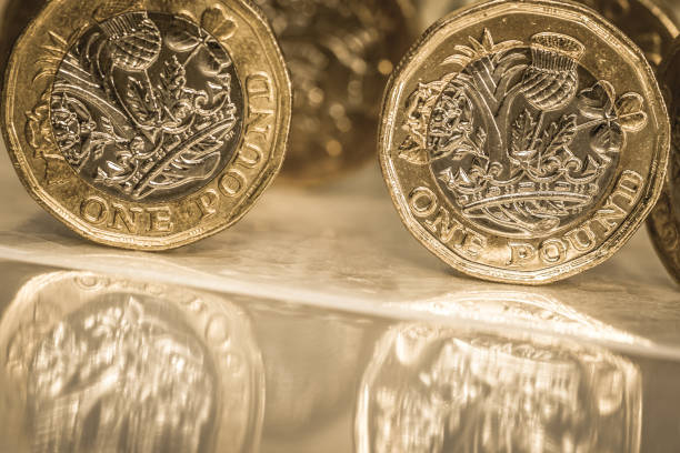 One pound coins sliding down a slope British one pound coins sliding down a sloping glazed tile. These are examples of the new bimetallic 12 sided edition that was introduced on 28 March 2017. british falling pounds stock pictures, royalty-free photos & images