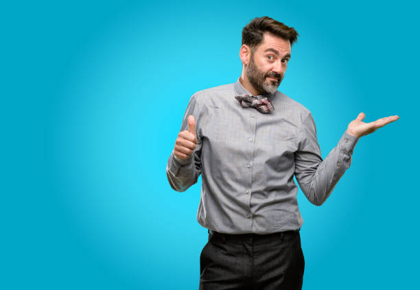 istock Middle age man, with beard and bow tie thumb up holding something in empty hand and making ok gesture 1043150356