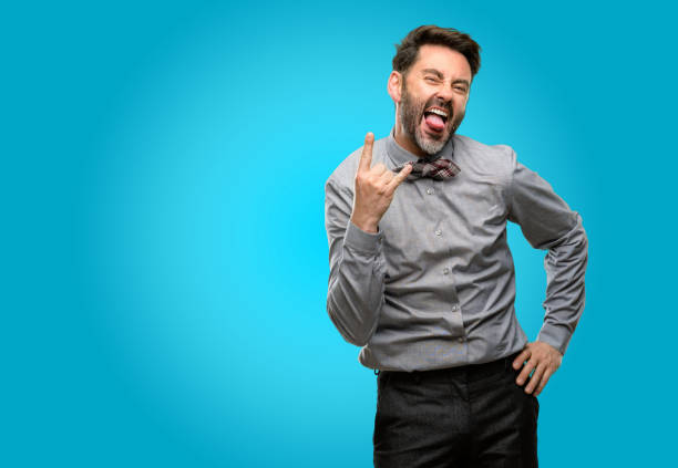 istock Middle age man, with beard and bow tie making rock symbol with hands, shouting and celebrating with tongue out 1043150442