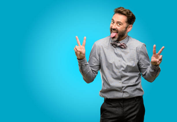 istock Middle age man, with beard and bow tie looking at camera showing tong and making victory sign with fingers 1043151506