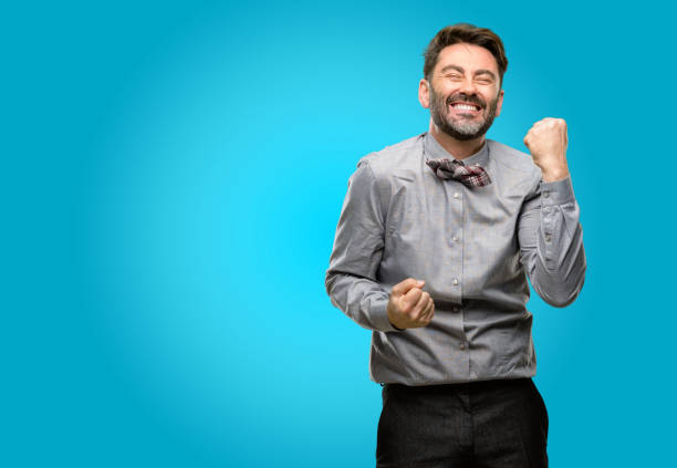 Middle age man, with beard and bow tie happy and excited celebrating victory expressing big success, power, energy and positive emotions. Celebrates new job joyful