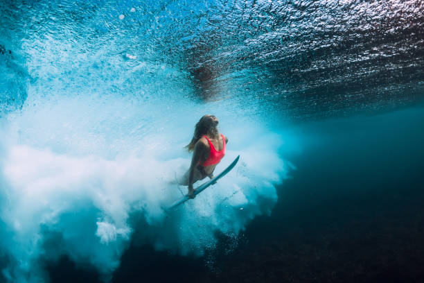 mujer de surfista con buceo tabla de surf bajo el agua con bajo la ola del océano. - bikini surfboard women surfing fotografías e imágenes de stock
