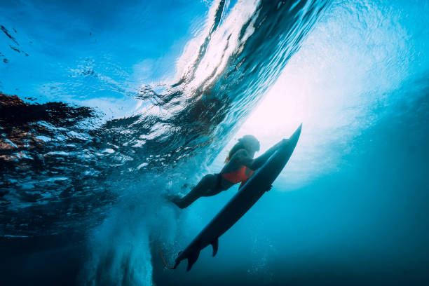 istock Surfer girl with surfboard dive underwater with fun under big ocean wave. 1043156302