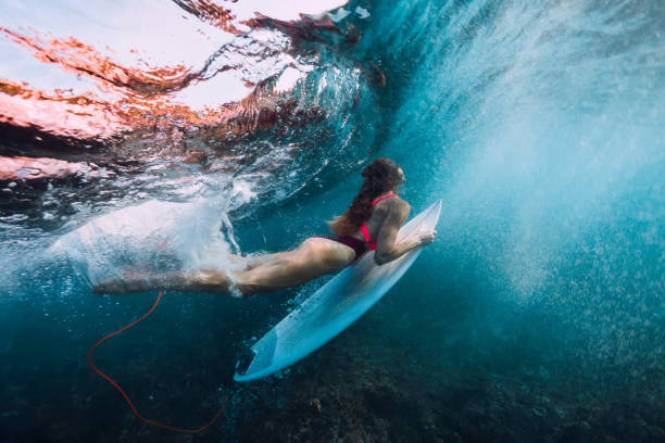 istock Surfer girl with surfboard dive underwater with under big wave. 1043156392