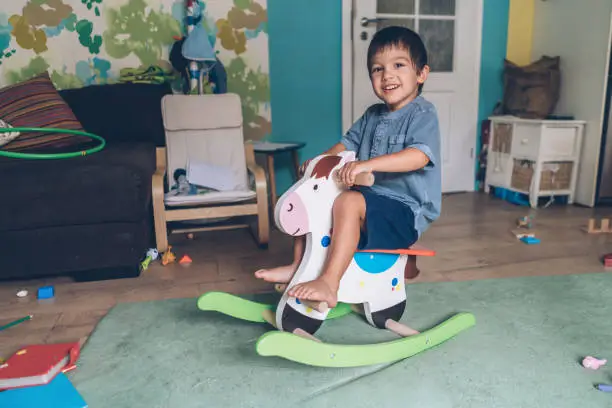 Little boy riding wooden rocking horse at home
