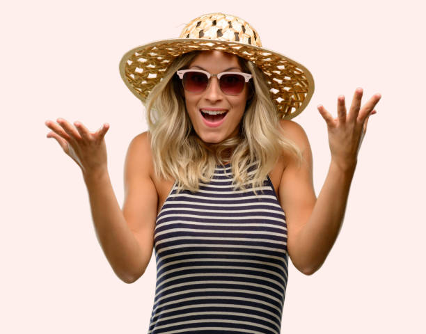 istock Young woman using sunglasses wearing summer hat happy and surprised cheering expressing wow gesture 1043169278
