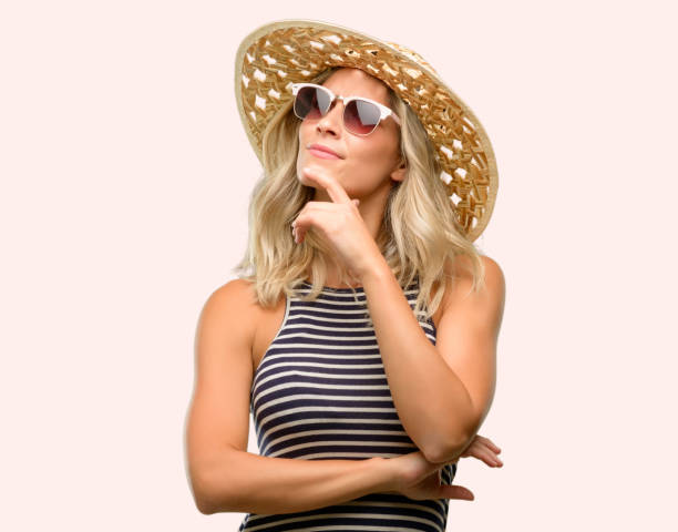 istock Young woman using sunglasses wearing summer hat thinking and looking up expressing doubt and wonder 1043169280