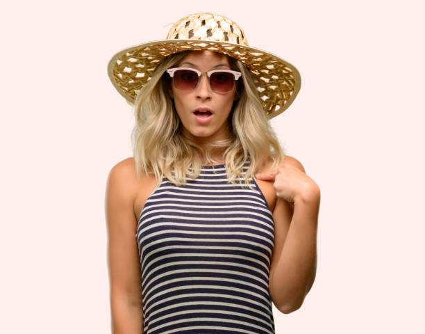 istock Young woman using sunglasses wearing summer hat happy and surprised cheering expressing wow gesture, pointing with finger 1043169310