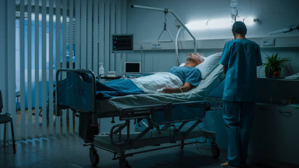 no hospital paciente sênior baseia-se na cama, enfermeira da ala faz check-up. recuperando o homem dormindo na ala do hospital moderno. - hospital ward - fotografias e filmes do acervo