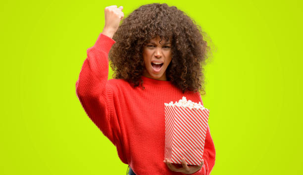 femme afro-américaine manger maïs soufflé agacé et frustré de crier avec colère, fou et crier à main levée, la colère concept - beautiful red hair curly hair human hair photos et images de collection