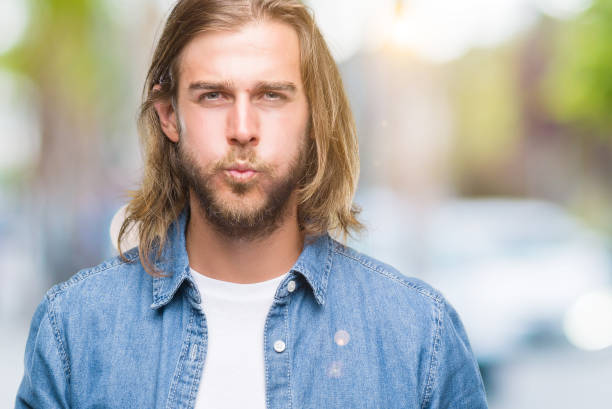 istock Young handsome man with long hair over isolated background puffing cheeks with funny face. Mouth inflated with air, crazy expression. 1043198232