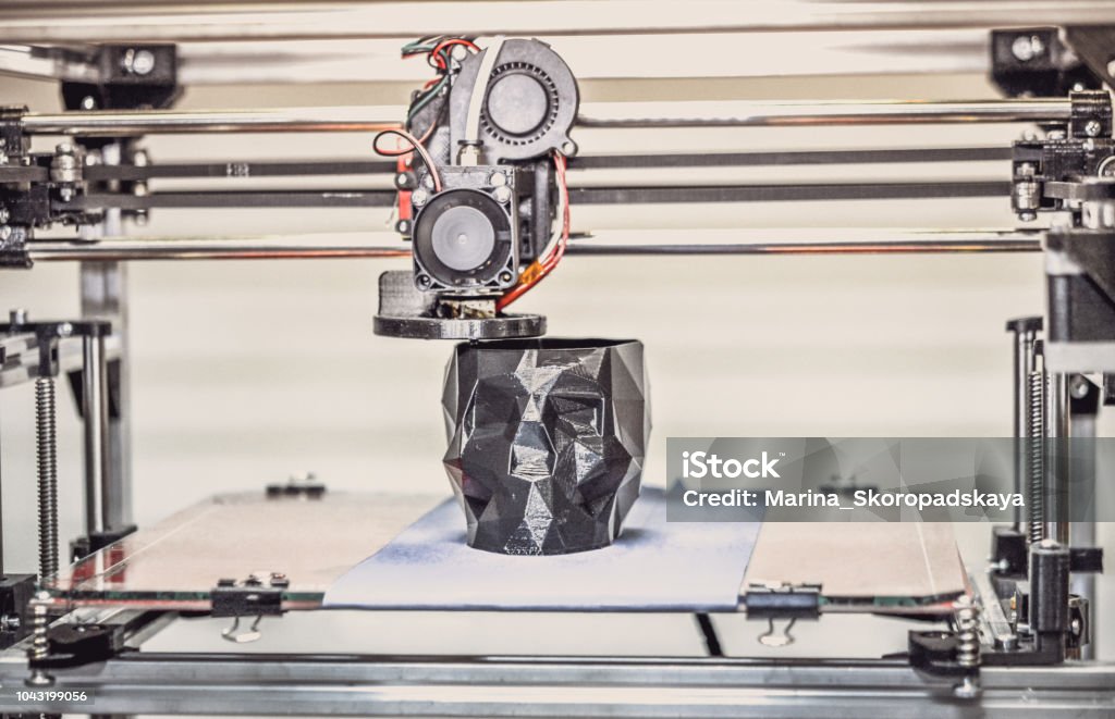 3D printer printing a model in the form of black skull close-up. 3D printer printing a model in the form of black skull close-up. The 4ht industrial revolution. Automatic three dimensional performs plastic modeling. Progressive modern additive technology Industrial Revolution Stock Photo