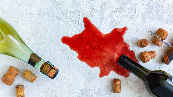 Spilled red wine, bottles, wine stoppers and corkscrew on textured white background. Top view.