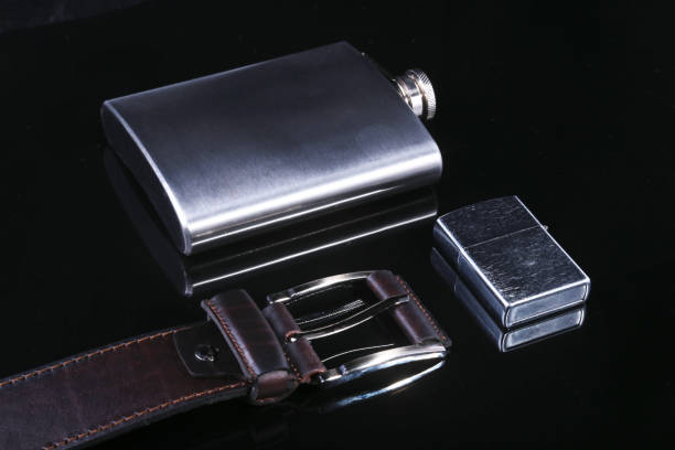 istock Stainless hip flask, lighter and luxury belt isolated on mirror black background. 1043212072