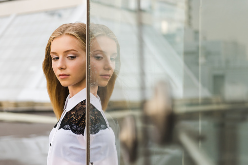 Portrait of girl with her glass reflection. Young blond female near transparent wall