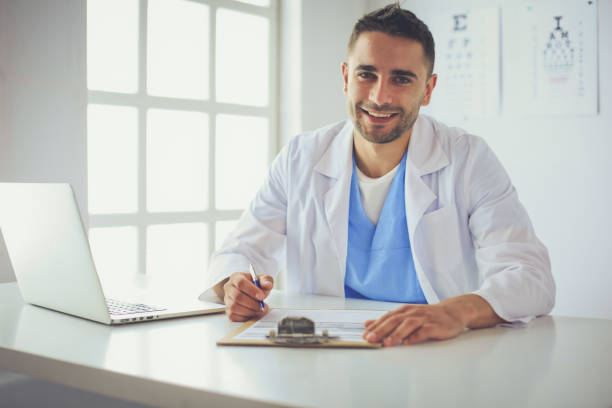 istock Male doctor using a laptop, sitting at his desk 1043219164
