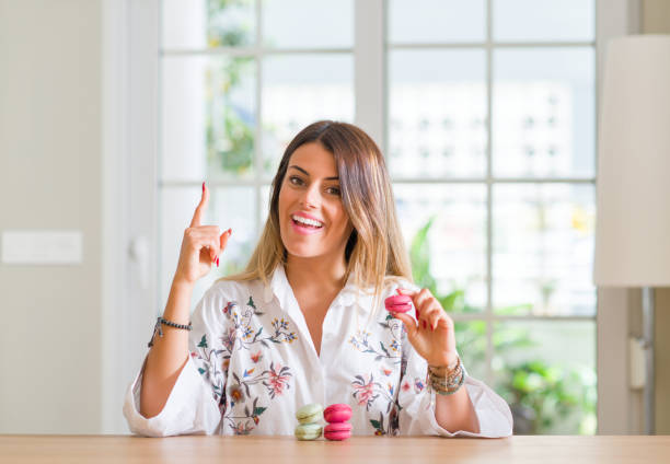 istock Young woman at home eating macarons surprised with an idea or question pointing finger with happy face, number one 1043223052