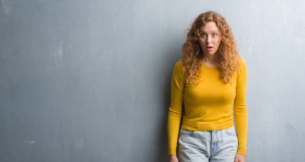 istock Young redhead woman over grey grunge wall scared in shock with a surprise face, afraid and excited with fear expression 1043231628