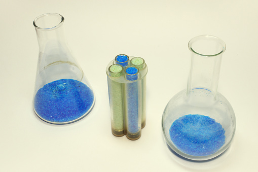 green and blue chemical salts in laboratory glassware: Erlenmeyer and Florence flasks, four test tubes in plastic holder